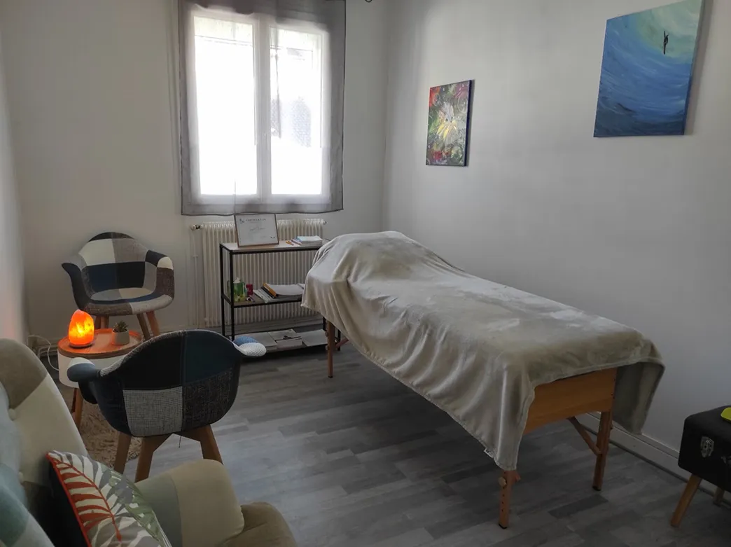L'espace de séance : la table de soin sous une couverture, deux fauteuils et une lampe de sel allumée.
