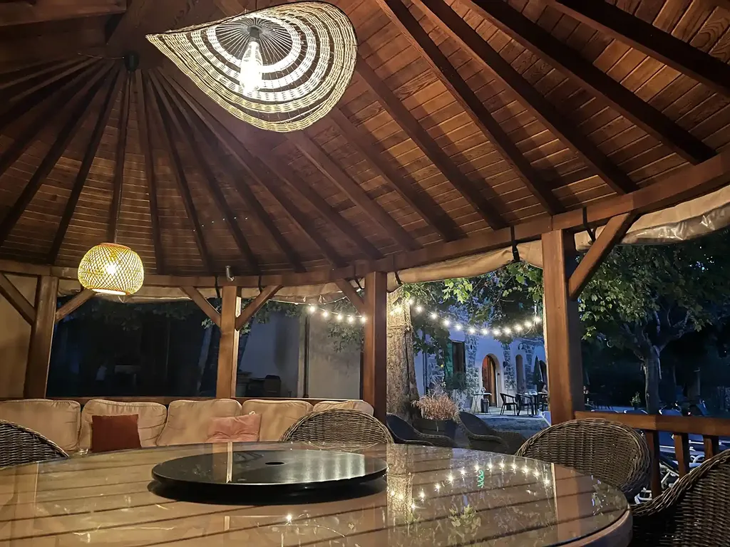 La terrasse couverte à la nuit tombée, guirlandes allumées sous la charpente en bois.